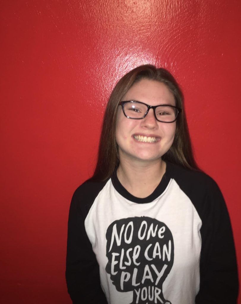 Female with glasses smiling in front of a red background